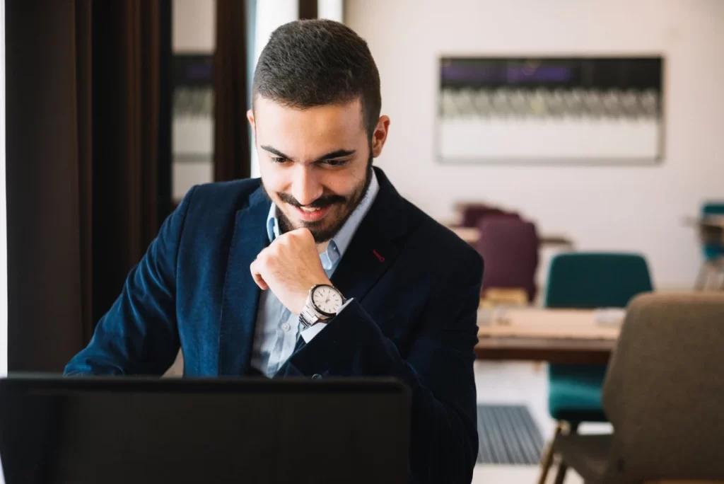 Homem sorridenet em um ambiente de escritório trabalhando em um laptop.