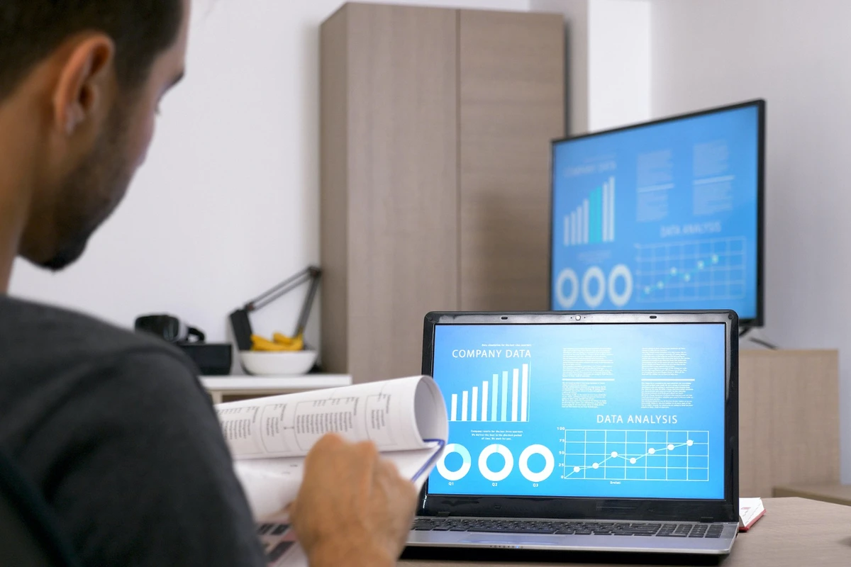 Homem analisando dados de negócios em computadores com gráficos e relatórios financeiros.