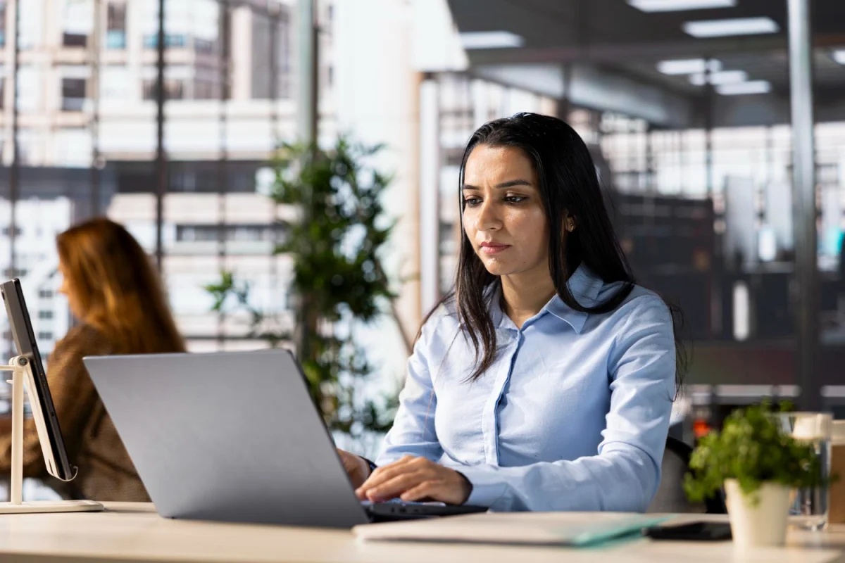 Mulher concentrada trabalhando em laptop em escritório moderno com plantas e luz natural